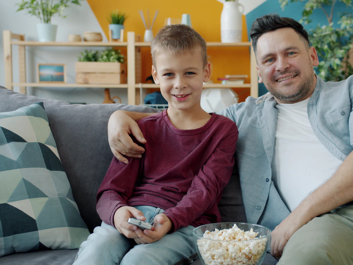 Father and son smiling together on the couch with a bowl of popcorn