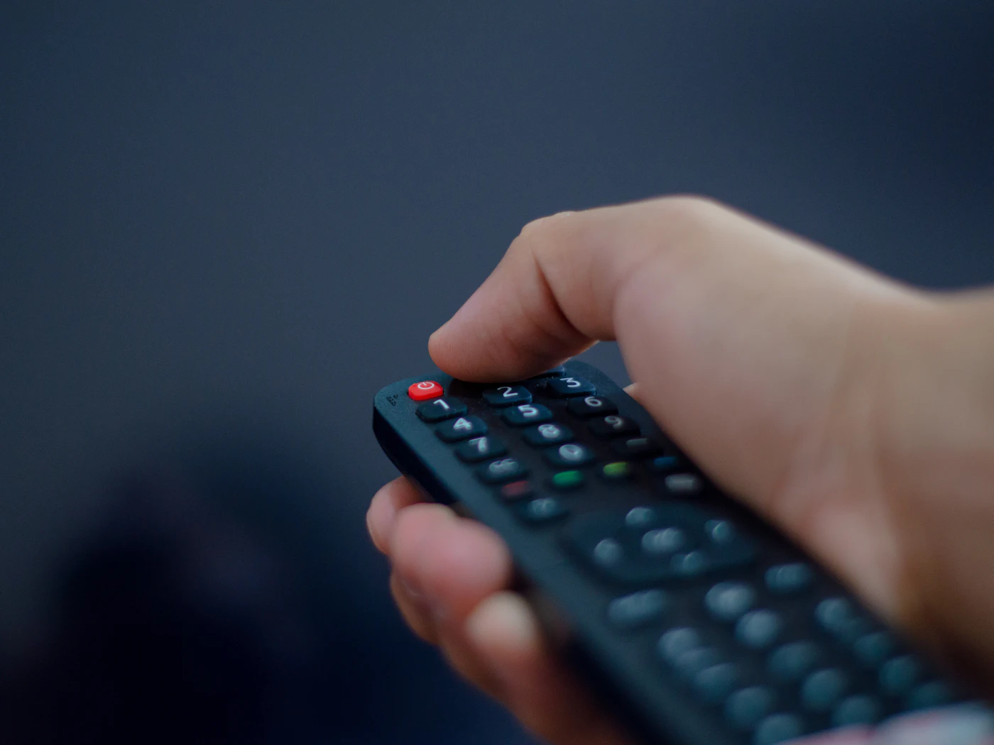 Close-up of a hand pointing a TV remote control in a dark room