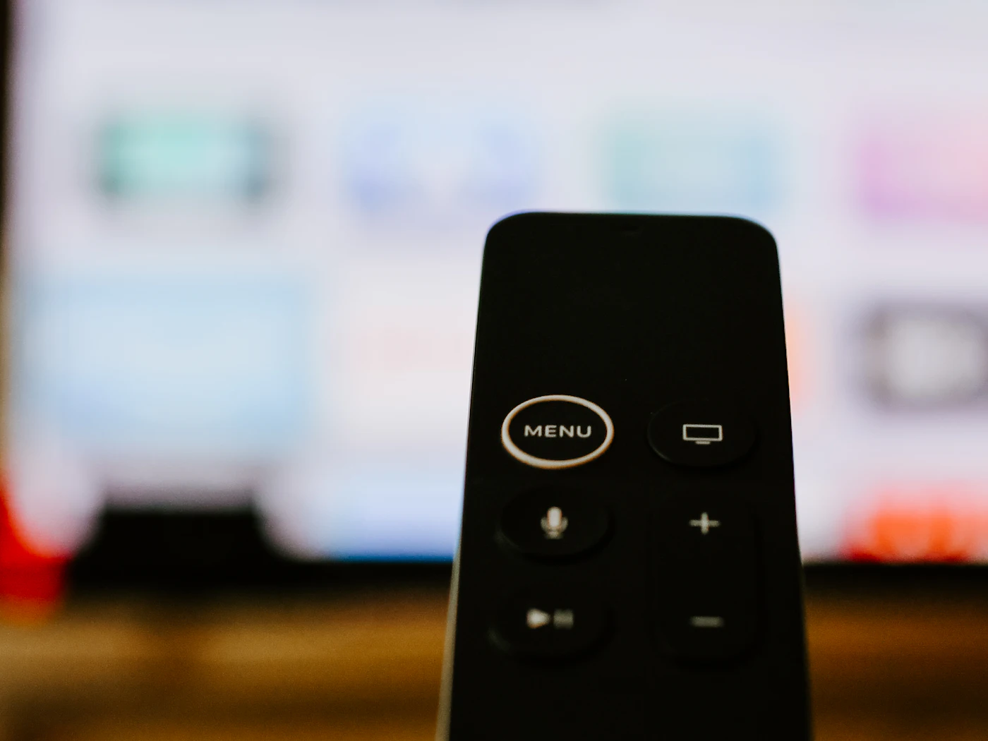 Black streaming remote held in front of a blurred TV app screen