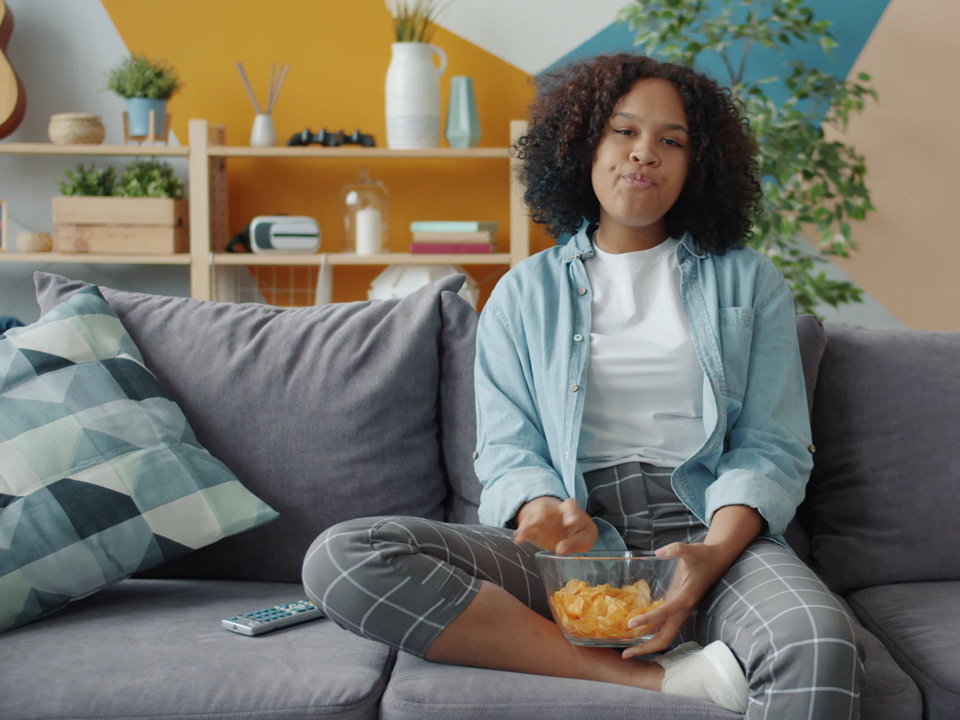 Young woman relaxing on a sofa with snacks while watching TV